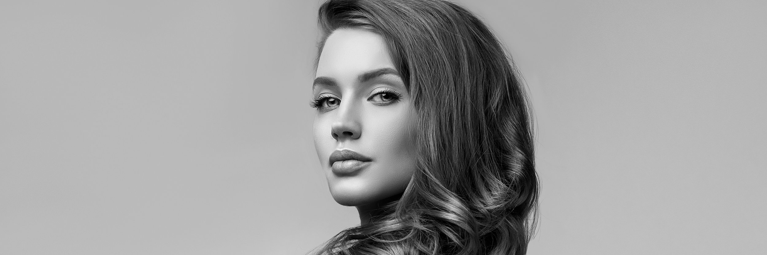 Black and white portrait of a woman with long wavy hair, looking over her shoulder.