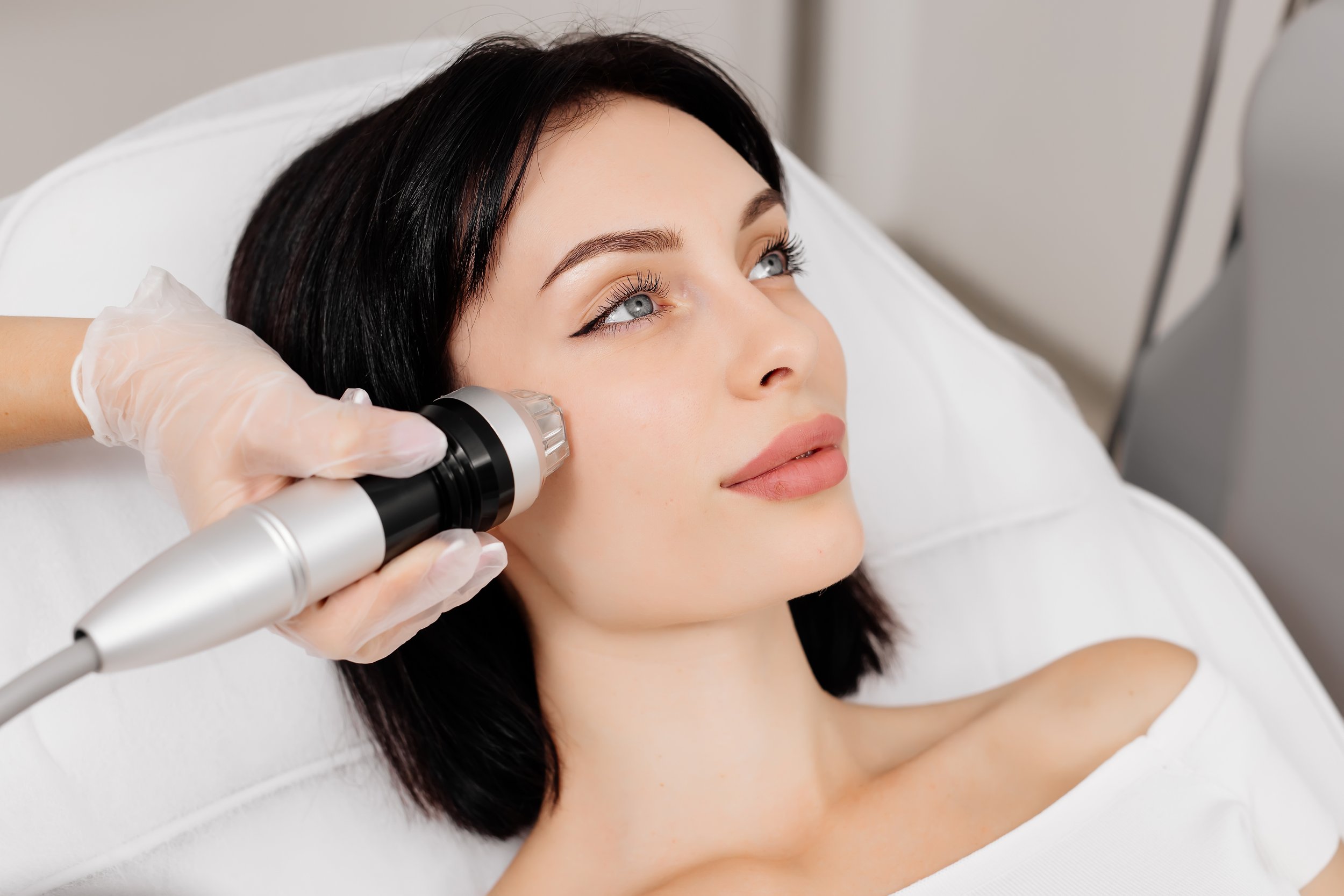 Woman receiving a facial treatment with a handheld device in a clinic